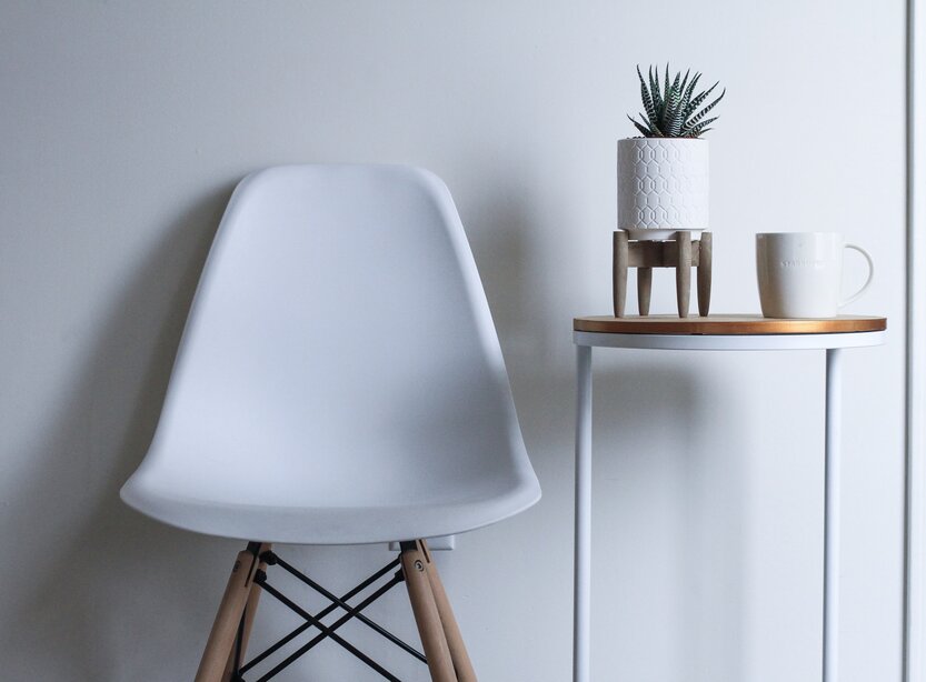Silla blanca junto a una mesa con una planta y una taza de estilo minimalista